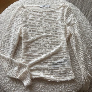 Vit långärmad topp från NA-KD - Säljer en stilren vit långärmad topp från NA-KD i ett unikt, texturerat material. Perfekt för att lägga till en intressant touch till din outfit. Toppen är i storlek XS och har en bekväm passform.