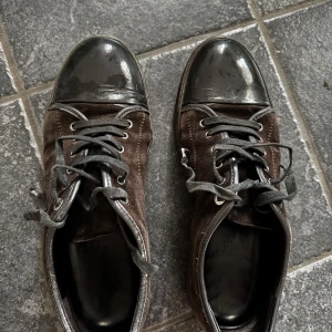 Lanvin skor - Snygga bruna sneakers med svarta blanka tåkappor och snörning. Skorna har en robust sula och är perfekta för en avslappnad stil. De är tillverkade i mocka och har en klassisk design som passar till många tillfällen.