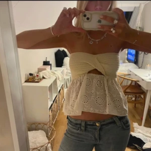 Vit axelbandslös topp - Säljer en söt vit axelbandslös topp med broderade detaljer och volang. Toppen har en knuten design framtill och är perfekt för varma dagar. Passar bra till jeans eller kjol för en avslappnad look. (Lånad bild)