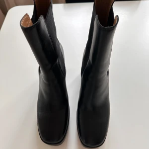 Svarta boots med klack - Snygga svarta boots i skinn från &Other Stories med hög klack och elastiska paneler på sidorna. Perfekta för en stilren look. De har en fyrkantig tå och är enkla att ta på och av.