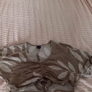 Blus med mönster - Beige blus med mönster. Löst åtsittande modell som är lite kortare. Justerbar längd framtill med snörning. Nästintill oanvänd. 