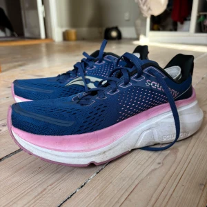 Blå och rosa löparskor från Saucony - Säljer ett par snygga löparskor från Saucony i blått med rosa/lila detaljer. Skorna har en luftig mesh-överdel och en tjock, dämpande sula för extra komfort. Skulle säga att de är hyfsat breda, jag som har normal bredd på mina fötter har lite utrymme kvar att röra fötterna med. Använt sparsamt, kanske ca 10-15 gånger. Säljer då de var för stora för mig! 