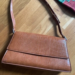 Liten väska  - Snygg brun axelväska från Monki. Väskan har en justerbar axelrem och stängs med magnetlås. Köptes för några år sedan men har inte riktigt kommit till användning !