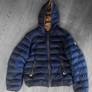 Blå pufferjacka från Colmar  - Snygg blå pufferjacka med huva och dragkedja framtill. Jackan har två fickor med dragkedjor och en broderad logga på ärmen. Perfekt för kyligare dagar. Den är fel markerad men skulle säga att det är en S-M. Den har dessa mått: 60cm * 50cm. Jackan har en mindre skada som har blivit fixat av en skräddare men är helt fungerande. Skriv gärna till mig om ni har några funderingar och priset kan diskut ras vid en snabb affär. 