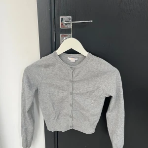 Grå kofta från Gina Tricot - Säljer en stilren grå kofta från Gina Tricot. Koftan har långa ärmar och knappar framtill. Perfekt för lager-på-lager under kyligare dagar. 🩶