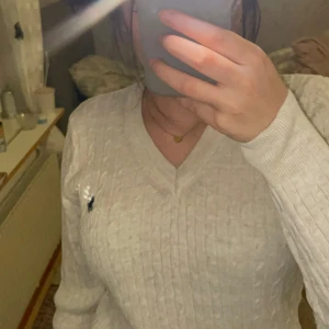 Vit stickad tröja från Ralph Lauren - Säljer en stilren vit stickad tröja från Ralph Lauren med v-ringning och det klassiska logotypbroderiet på bröstet. Tröjan har långa ärmar och en ribbad struktur som ger en snygg passform. Perfekt för kyligare dagar!