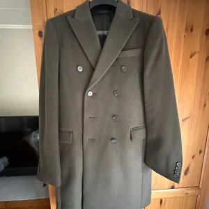 Grön-brun kappa/rock  - Snygg brun kappa med dubbelknäppning och klassisk krage.  Perfekt för kyligare dagar. Storlek 50 så passar typ M