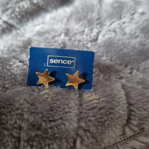 Guldstjärna örhängen från Sence - Snygga örhängen i form av stjärnor från Sence. De är i en elegant guldton och perfekta för att ge en extra touch till din stil. Passar både till vardag och speciella tillfällen.