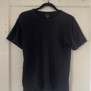 Svart t-shirt från Newbody - Säljer en klassisk svart t-shirt från Newbody i storlek S. Den är gjord av 100% bomull vilket gör den superbekväm och perfekt för vardagsbruk. T-shirten har en normal passform och korta ärmar. Perfekt basplagg att ha i garderoben!