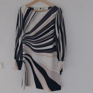 Mönstrad klänning från Richard Allan x H&M - Säljer en superfin klänning från Richard Allan x H&M i storlek 40. Den har ett coolt mönster i svart, beige och vit med långa ärmar och snygga knappar vid ärmsluten. Perfekt för både vardag och fest!