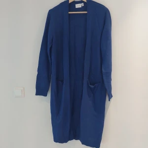 Blå kofta från VILA - Säljer en snygg och bekväm blå kofta från VILA. Den är lång och har långa ärmar, perfekt för kyliga dagar. Koftan är i ett mjukt material som känns skönt mot huden. Den har en enkel och stilren design utan knappar, vilket gör den lätt att matcha med olika outfits. Perfekt för både vardag och lite finare tillfällen!