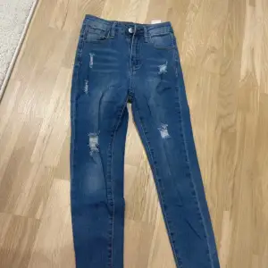 Säljer ett par snygga blå jeans med slitningar. De har en hög midja och en skinny passform som sitter riktigt bra. Perfekta för en casual look! 