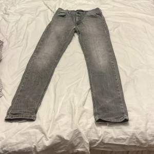 Grå jeans från Replay Wally’s slim - Snygga grå jeans från Replay med en klassisk femficksdesign. De har en diskret tvättad look och är perfekta för en avslappnad stil. Märkeslogga på baksidan och knappgylf framtill.
