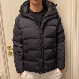 Svart dunjacka från Massimo Dutti - Säljer en stilren svart dunjacka från Massimo Dutti. Jackan har en praktisk huva och dragkedja framtill. Perfekt för kyliga dagar. Modell 180cm. Priset är förhandlingsbart vid snabb affär.