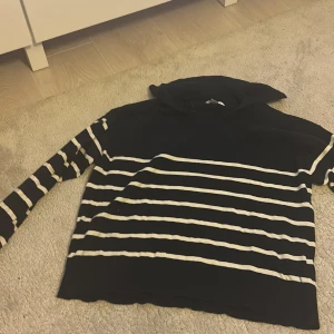 Svart och vit randig tröja från Gina Tricot - Säljer en svart och vit randig tröja från Gina Tricot. Tröjan har långa ärmar och en hög krage som ger en stilren look. Perfekt för kyligare dagar.