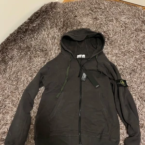 Stone island zip hoodie mörkgrå - Säljer nu en riktigt fin rep stone island zip hoodie i en jättefin mörkgrå färg. Storleken är M och hoodien är helt ny, enda bristen är att ena snörets stickning har gått upp men det är inte så mycket (syns på sista bilden)