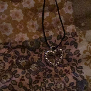 Halsband med hjärtberlock - Snyggt halsband med en hjärtformad berlock i silverfärg. Berlocken är dekorerad med små pärlor som ger en elegant touch. Perfekt för att ge en romantisk känsla till din outfit.
