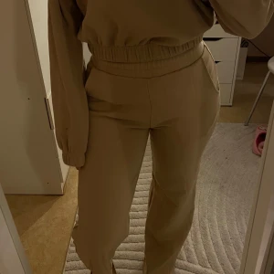 Beige sweatshirt med matchande byxor - Säljer en beige croppad sweatshirt med dragkedja och hög krage tillsammans med matchande mjukisbyxor. Från bikbok. 