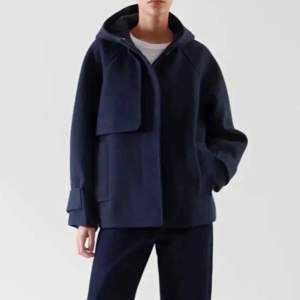Säljer en stilren mörkblå kappa från COS. Jackan har en minimalistisk design med knappar framtill och långa ärmar. Perfekt för en elegant look. Nypris var runt 2200 (minns ej exakt)