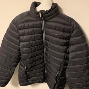 Svart vinter/pufferjacka från Tuxer - Säljer en svart pufferjacka från Tuxer med dragkedja och hög krage. Jackan har långa ärmar och två praktiska fickor med dragkedjor. Perfekt för kyliga dagar och som skidjacka. Storlek M.