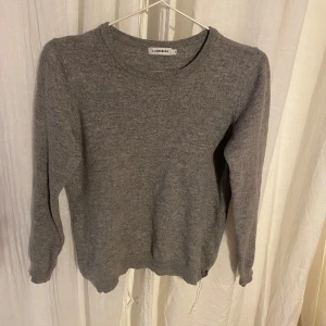 Stickad grå tröja från J.Lindeberg - Säljer en stilren grå tröja från J.Lindeberg. Tröjan är långärmad och har en klassisk rund halsringning. Den är från början kvinna medium men har både krympt och har en mer unisexfigur. Det var ett litet hål där sömmen gått upp men det är nu ihopsytt(bild nr5).Perfekt för kyligare dagar och enkel att matcha med olika outfits. Tröjan är i en cashmere och merinoblandning. Nypris ca 1500:- så passa på att fynda denna snygga tröja!