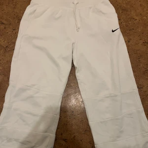 Vita mjukisbyxor från Nike - Snygga vita mjukisbyxor från Nike med en diskret logga på benet. Byxorna har en bekväm resårmidja med snörning för justerbar passform. Perfekta för en avslappnad stil.