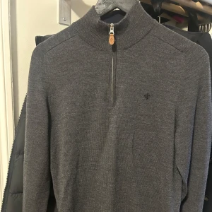 Grå tröja med dragkedja från Morris - Säljer en stilren grå tröja från Morris med halv dragkedja och hög krage. Tröjan har ett diskret broderat emblem på bröstet och är perfekt för kyligare dagar. Passar både till vardags och mer uppklädda tillfällen.