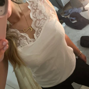 Vit ärmlös topp med spetsdetaljer - Säljer en stilren vit topp med vacker spetsdetalj vid halsringningen. Toppen är ärmlös och har en elegant passform som passar perfekt till både vardag och fest💕💕