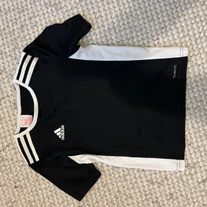 Svart och vit fotbollströja från Adidas - Säljer en svart och vit fotbollströja från Adidas med korta ärmar och klassiska ränder på axlarna. Tröjan har Climacool-teknologi för optimal ventilation under träning. .