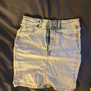 jeanskjol - Säljer en snygg ljusblå jeanskjol från Gina Tricot i modellen Molly. Kjolen har en klassisk design med dragkedja och knapp framtill samt fickor. Perfekt för en avslappnad stil.