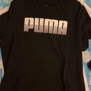 Svart t-shirt från Puma - Snygg svart t-shirt från Puma med ett stort vitt logotryck på framsidan. Perfekt för en sportig look eller avslappnad stil. Tillverkad i mjukt material för extra komfort. Inga difekter precis som ny!