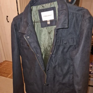 Svart jacka från Blend - Säljer en stilren svart jacka från Blend. Jackan har en dragkedja framtill och en knappdetalj på bröstfickan. Perfekt för höst och vår med sin klassiska design och bekväma passform.