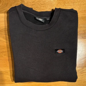 Svart tröja från Dickies - Säljer en svart tröja från Dickies med rund hals och ribbade muddar. Perfekt för en stilren och avslappnad look. Tröjan har en liten logotyp på bröstet. Tveka inte att höra av dig!
