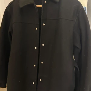 Svart kappa från Vero Moda - Säljer en stilren svart kappa från Vero Moda i storlek XS, men den är rymlig i modellen och passar även dig som vanligtvis bär S. Kappan har en klassisk krage och knäppning framtill, vilket gör den till ett perfekt val för en elegant och tidlös look.