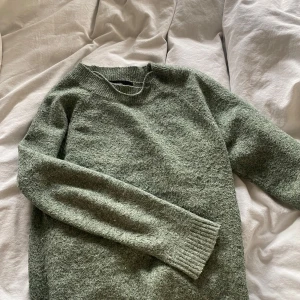 Grön stickad tröja - Mysig grön stickad tröja med rund hals och långa ärmar. Tröjan har en enkel design med ribbade muddar vid ärmslut och nederkant.