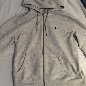 Grå hoodie från Ralph Lauren - Säljer en stilren grå hoodie från Ralph Lauren med dragkedja och broderad logga på bröstet. Storlek M. Köpt på Room 1006 på Emporia Malmö. Mycket bra skick. 