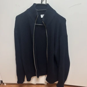 Svart stickad kofta med dragkedja - Säljer en stilren svart stickad kofta med dragkedja. Perfekt för kyliga dagar med sin ribbade design och långa ärmar. En klassisk och mångsidig tröja för garderoben. Storlek Small men funkar även för Medium säljs för 600kr