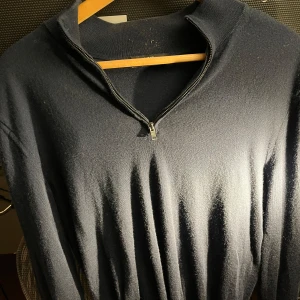 Mörkblå tröja i merinoull från Mango - Säljer en stilren mörkblå tröja från Mango i mjuk merinoull. Tröjan har en praktisk dragkedja vid halsen och långa ärmar. Perfekt för kyligare dagar och ger en snygg look till vardagsoutfiten. Fråga så kommer fler bilder!