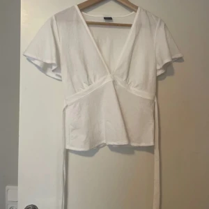Vit omlottopp från Gina Tricot - Snygg vit omlottopp från Gina Tricot med korta ärmar och knytband i midjan. Perfekt för en stilren look, lätt att matcha med jeans eller kjol. Använd 3 gånger max. 💗💗