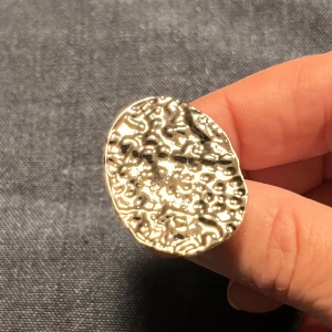 Silverfärgad ring med textur - Unik silverfärgad ring med en stor, oval platta och texturerad yta. Ringen har en justerbar design för att passa olika storlekar. Perfekt för att ge en stilfull touch till din outfit.