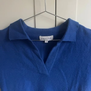 Blå tröja från Davida - Snygg blå tröja från Davida i cashmere. Tröjan har korta ärmar och en klassisk krage, perfekt för en stilren look. Väldigt bra skick🫶🏻Köptes för över 1500kr, säljer för 550kr + frakt