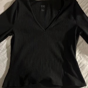Svart ribbad topp  - Snygg svart ribbad topp från 157 med v-ringning. Perfekt för en stilren look. Toppen har långa ärmar och en skön passform.