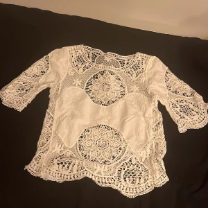 Vit spetsblus från SHK Mode - Säljer en elegant vit spetsblus från SHK Mode med vackra virkade detaljer. Blusen har trekvartsärmar och ett unikt mönster som ger en bohemisk känsla. Perfekt för att lyfta vilken outfit som helst!