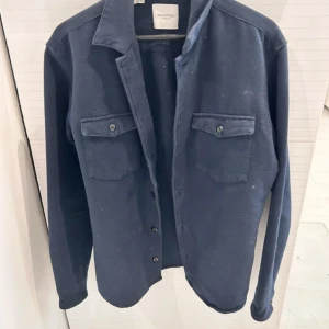 Blå overshirt från Selected Homme - Säljer en stilren blå overshirt från Selected Homme. Perfekt för lager-på-lager-stil. Passar bra till både casual och mer uppklädda tillfällen.