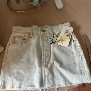 Vit jeanskjol från Levi's - Säljer en snygg vit (jätte ljusblå) jeanskjol från Levi's. Kjolen har en knappgylf och är perfekt för en avslappnad stil. Den är i en kort modell och passar perfekt till sommaren. Den är aldrig använd med lappar kvar!!🤍