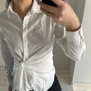 Vit knytblus - Säljer en vit blus med knytning framtill. Blusen har långa ärmar och knappar hela vägen ner. Perfekt för en chic och avslappnad look.