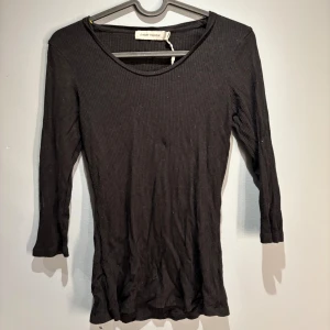 Svart ribbad topp från Carin Wester - Säljer en stilren svart ribbad topp från Carin Wester. Toppen har trekvartsärmar och en rund halsringning, perfekt för en enkel och elegant look. Passar bra till både jeans och kjol.