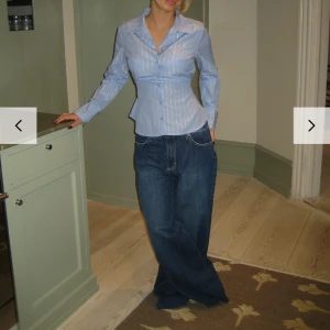 Blå randig skjorta med knytband - Snygg blå skjorta med vita ränder och knytband i midjan för en figurnära passform. Endast testas, har prislappen kvar. Hann inte returnera i tid. Storlek: xs/s. Kostar 544kr+ frakt på deras hemsida. 