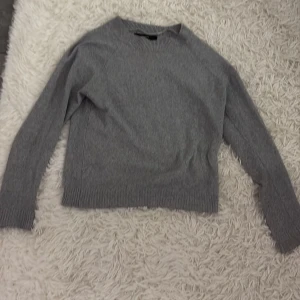 Grå stickad tröja - Säljer en stilren grå stickad tröja med långa ärmar. Perfekt för kyligare dagar och enkel att matcha med olika outfits. Tröjan har ribbade muddar vid ärmslut och nederkant för en bekväm passform.