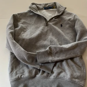 Ralph lauren halfzip  - Säljer en stilren grå tröja från Polo Ralph Lauren med dragkedja vid halsen och det klassiska broderade logotypen på bröstet. Perfekt för en avslappnad och snygg look. Tröjan har långa ärmar och är tillverkad i ett mjukt material. Scick är en 8 då det finns lite små tecken på användning priset är ej hugget i sten.
